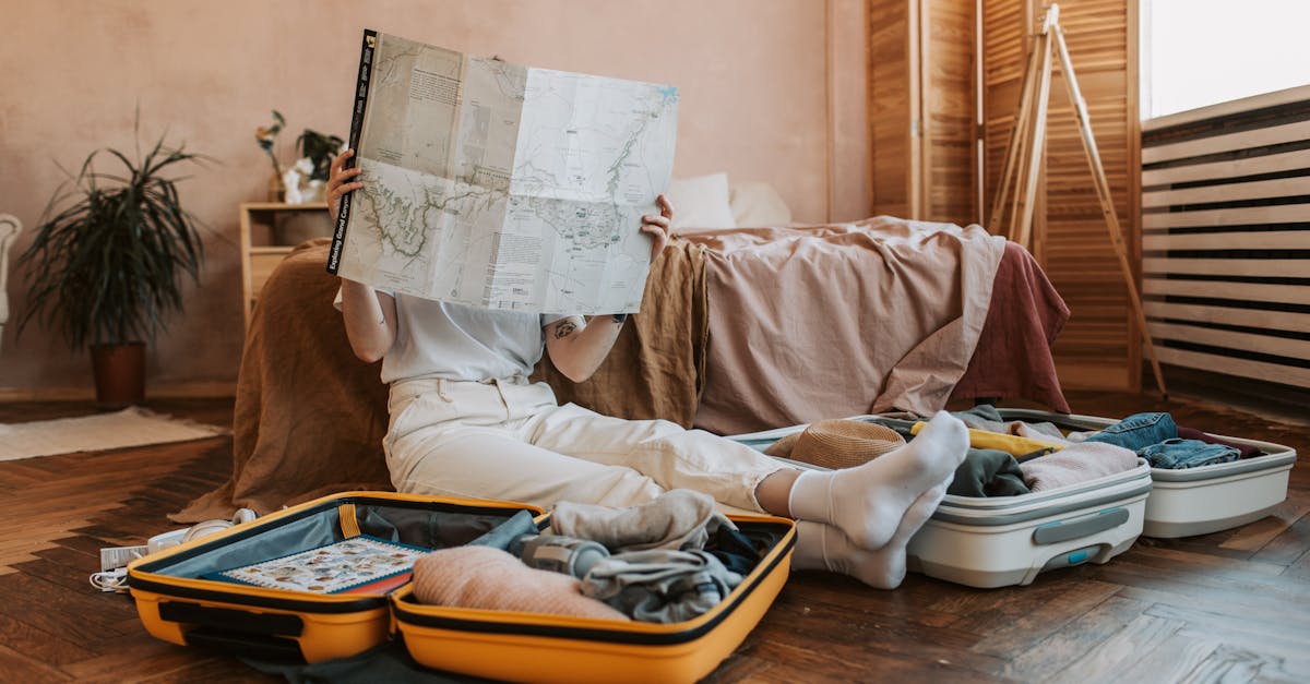 Person packing suitcases with a map in a cozy bedroom, preparing for a journey.
